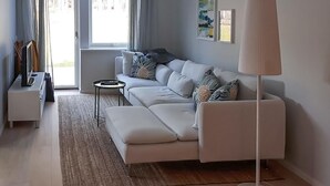 A modern living room with a white sofa, a side table, and a floor lamp. There is a window with curtains, a painting on the wall, and a small rug on the floor. - Nice home in Västervik with WiFi (Västervik)