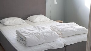A neatly made bed with white bedding in a room with a grey headboard and a small bedside table with a lamp. - Nice home in Västervik with WiFi (Västervik)