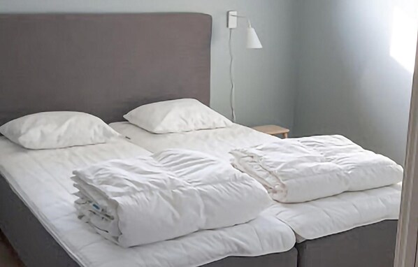 A neatly made bed with white bedding in a room with a grey headboard and a small bedside table with a lamp. - Nice home in Västervik with WiFi (Västervik)