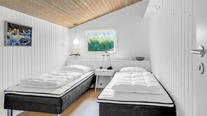 A room with two single beds, a small desk, a window with a view of greenery, and a painting on the wall.