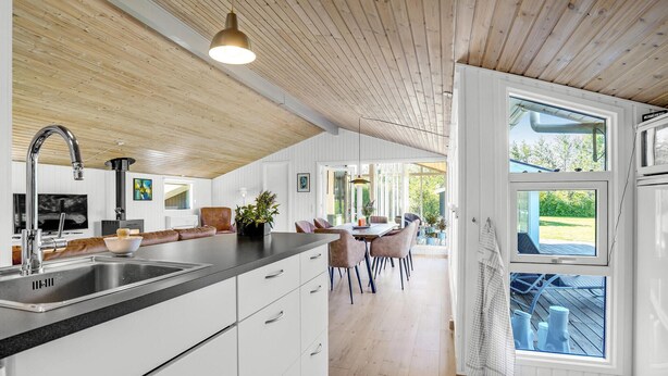 A modern kitchen with a wooden ceiling, white cabinetry, and a large window.