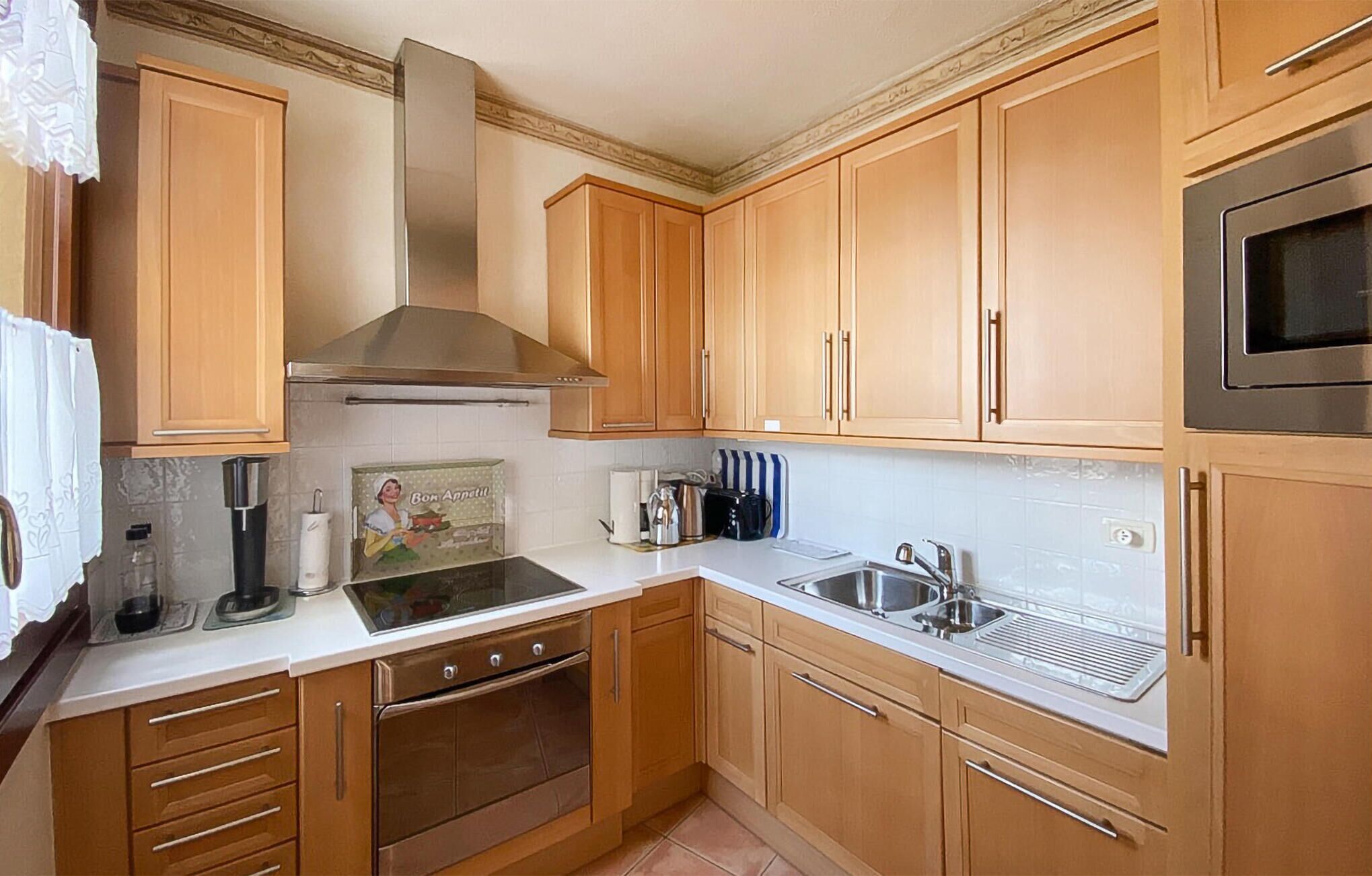 A kitchen with wooden cabinets, a stainless steel range hood, a built-in oven, a sink, and a microwave.
