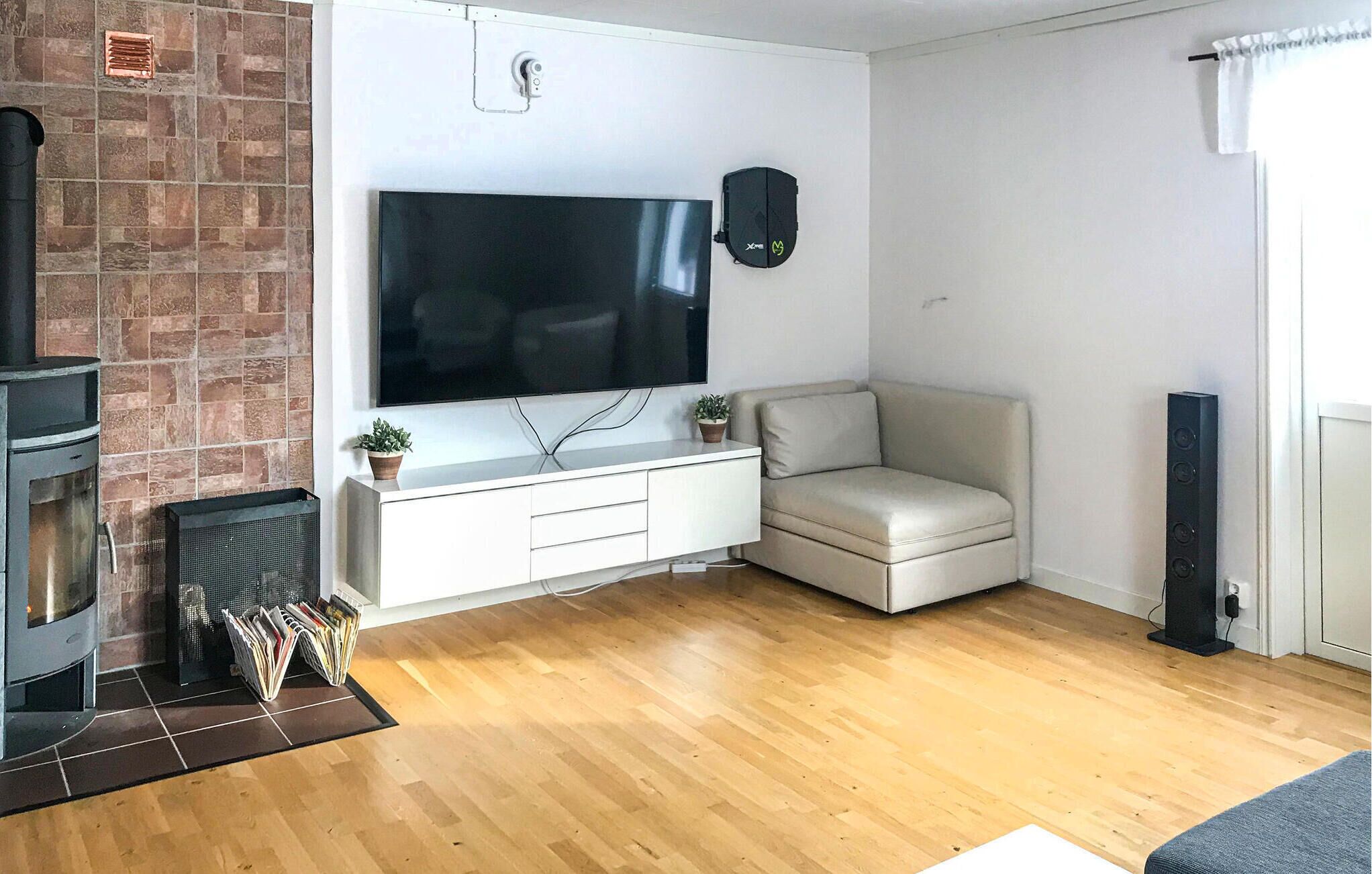 A living room with a flat-screen TV mounted on the wall, a white entertainment unit, a beige sofa, a fireplace, and a radiator.