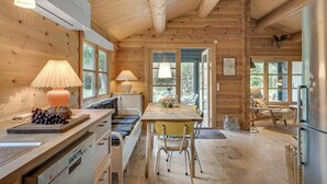 A cozy cabin interior with a wooden dining table, chairs, a sofa, and a kitchen area with a refrigerator. - Nice home in Hornbæk with WiFi (Hornbæk)