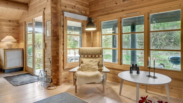 A cozy cabin interior with wooden walls, a plush chair, a small table, and large windows offering a view of greenery. - Nice home in Hornbæk with WiFi (Hornbæk)