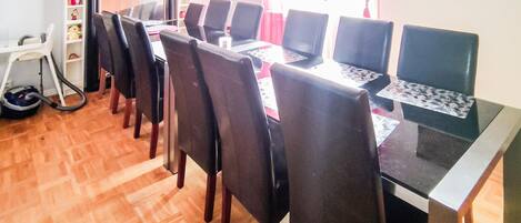Un comedor con una mesa larga, varias sillas y un aspirador cerca de la entrada.