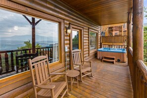Relax on the deck with a hot tub, Adirondack chairs, and a bench, taking in the views of the surrounding mountains and trees.