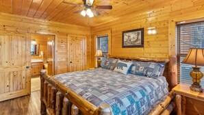 Un dormitorio de cabaña de madera con una cama de madera, un ventilador de techo y un cuadro en la pared.