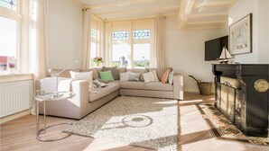 A living room with a beige sofa, a glass coffee table, a fireplace, and large windows with curtains. - Stunning home in Bergen aan Zee (Bergen aan Zee)