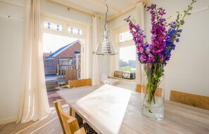 Een eethoek met een houten tafel en stoelen, een bloevas en uitzicht op een gebouw.