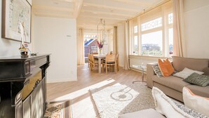 A spacious living room with a fireplace, a dining area with a table and chairs, and large windows with curtains. - Stunning home in Bergen aan Zee (Bergen aan Zee)