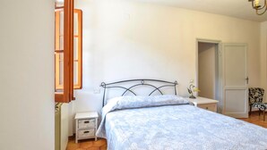 Un dormitorio con cama, mesita de noche, lámpara, silla y puerta.