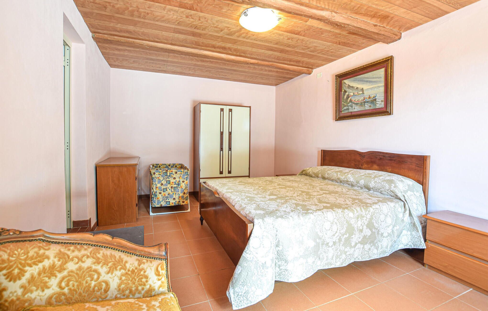 A bedroom with a bed, wooden wardrobe, a chair, and a painting on the wall.