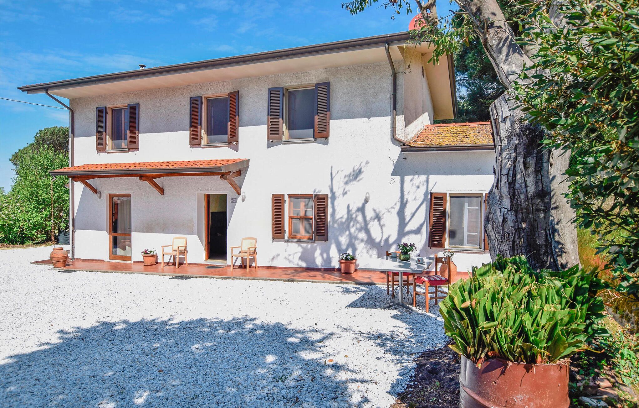 A two-story house with a covered patio, outdoor seating, and a gravel driveway.