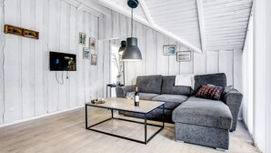 Un loft moderne avec des poutres en bois apparentes, un canapé d’angle gris, une table basse en verre et un téléviseur à écran plat fixé au mur.