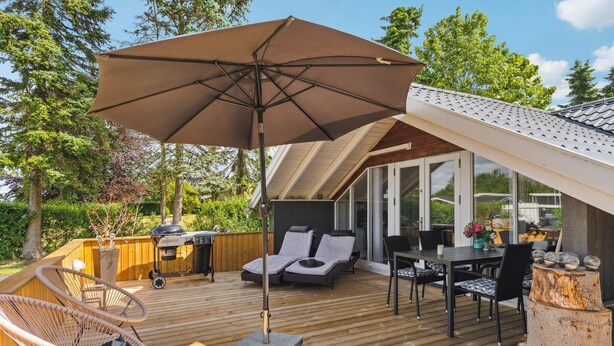 Une terrasse dotée de mobilier d’extérieur, d’un barbecue et d’un grand parasol.