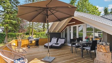 Una terraza con mobiliario exterior, una parrilla y un gran paraguas.