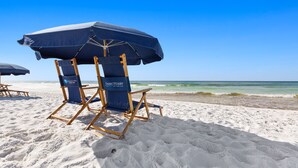 Een strand met een blauwe strandstoel en parasol, en een houten stoel.