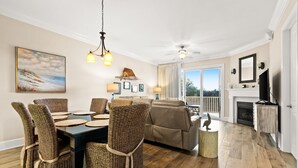 Een ruime woonkamer met een eethoek, een open haard en een groot raam met uitzicht op de omgeving.