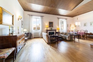 A spacious living room with a wooden ceiling, a fireplace, a sofa, a dining table, and a bench.