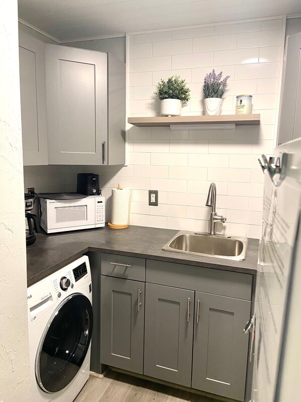 A compact kitchen with a washing machine, microwave, and a sink.
