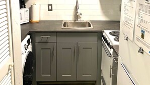 Uma cozinha compacta com armários cinza, uma pia de aço inoxidável, forno embutido e geladeira.