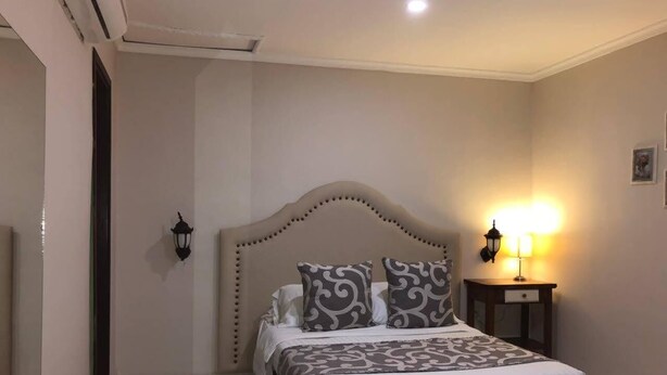 Un dormitorio con una cama grande, una mesita de noche con lámpara y una lámpara de pared.