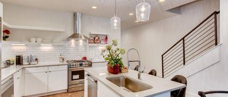 A modern kitchen with white cabinetry, a stainless steel stove, and pendant lighting.