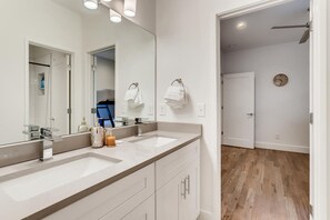 Een moderne badkamer met twee wastafels, een grote spiegel en een douchecel zichtbaar door een geopende deur.