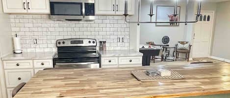 Una cocina con armarios blancos, una isla grande con taburetes de bar, un microondas y una lámpara colgante.