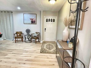 A living room with a wooden floor, a white door, a coat rack, and a framed picture on the wall. - Displaced Families Ready | Sleeps 10 | Pets OK | EV Charger (Decatur)