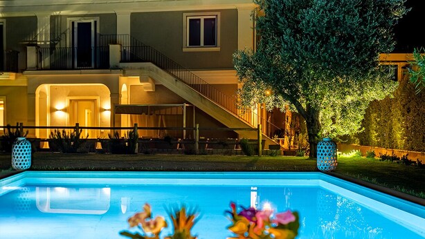 Une piscine avec une terrasse en bois, des plantes en pot et un escalier menant à un bâtiment.