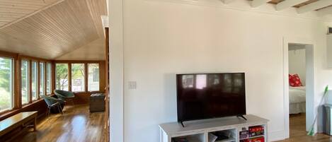 Una habitación amplia con suelo de madera, un televisor de pantalla plana grande sobre un pedestal blanco y un banco a lo largo de la pared.