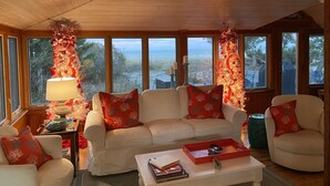 Ein gemütliches Wohnzimmer mit einem weißen Sofa, roten Zierkissen, einem Couchtisch mit Büchern und einem Weihnachtsbaum.