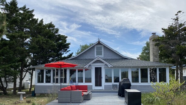 Ein Haus mit überdachter Veranda, einem roten Regenschirm und Sitzgelegenheiten im Freien.