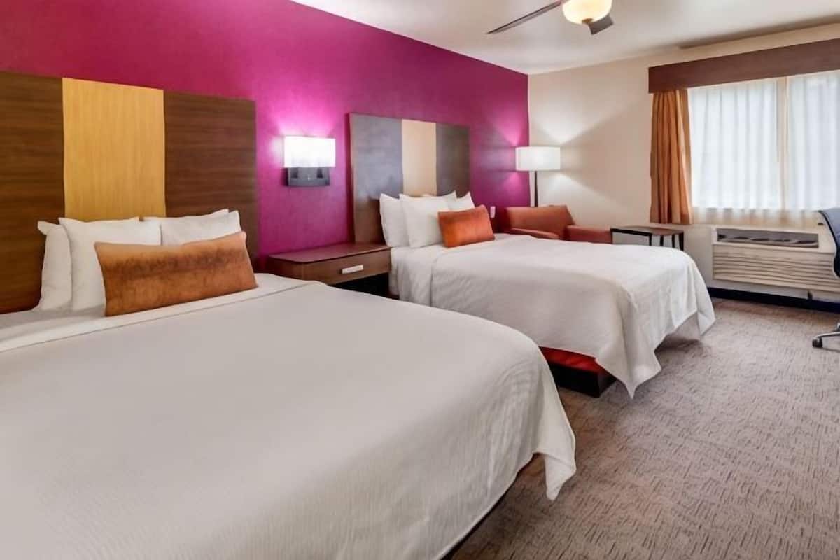 A hotel room with two beds, a desk, a chair, a lamp, and a window with curtains.