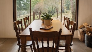 A dining area with a large table, wooden chairs, a potted plant, and a view of a garden through large windows. - Top of the Otways - Nature Lodge (Barramunga)