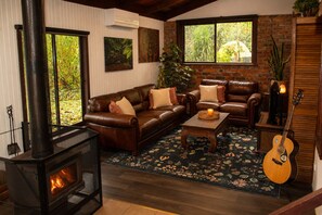 A cozy living room with a fireplace, leather sofas, a coffee table, and a guitar. - Top of the Otways - The Nature Lodge (Barramunga)