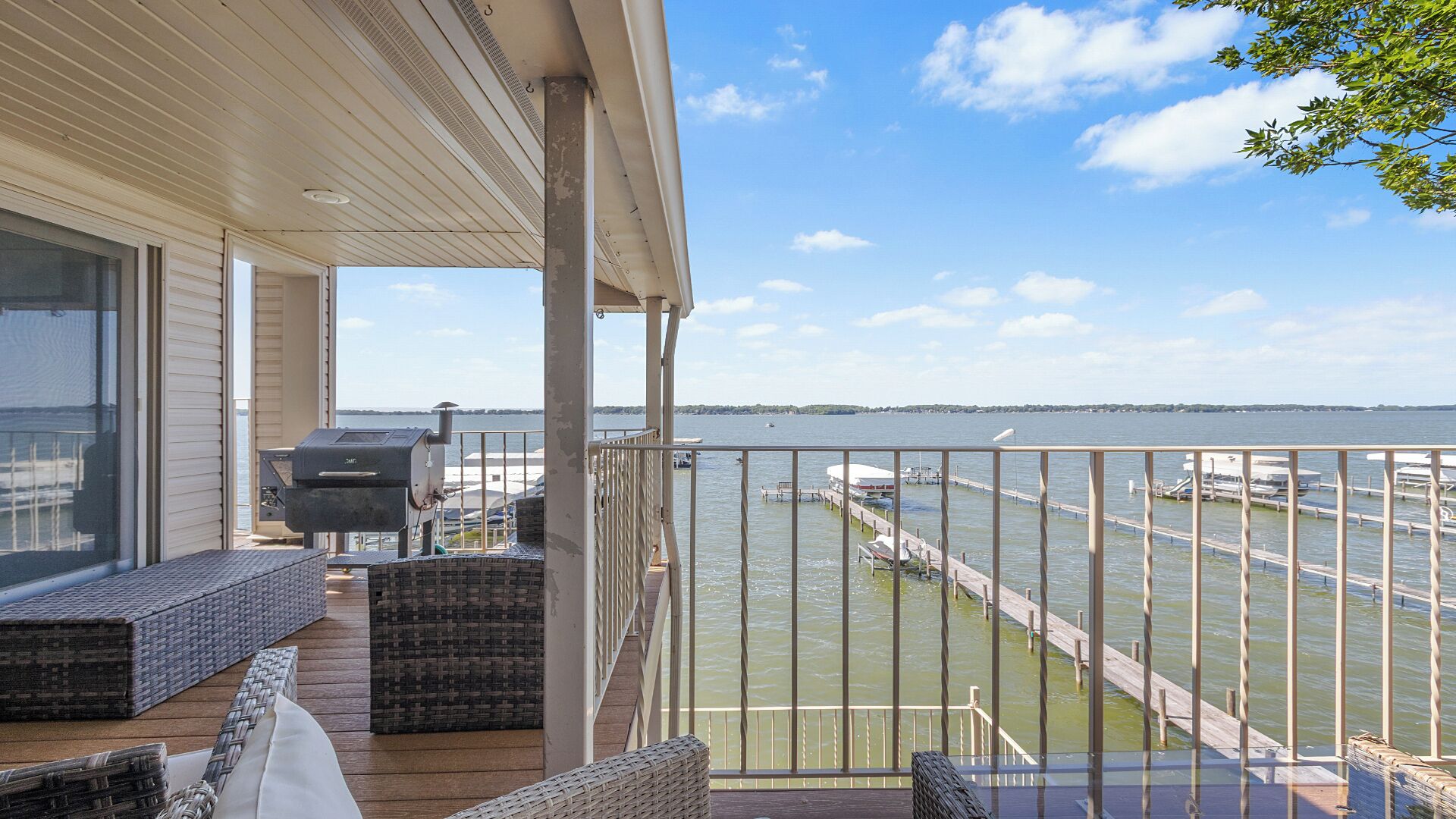 A balcony with wicker furniture, a grill, and a view of a marina with docks and boats.