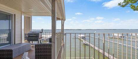 A balcony with wicker furniture, a grill, and a view of a marina with docks and boats.