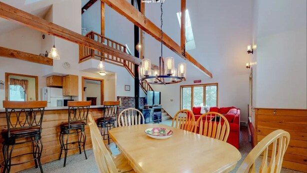 A spacious dining area with a wooden table and chairs, a kitchen in the background, and a staircase leading to an upper level. - Walk to pond / playground in pet friendly chalet while enjoying mountain views (Madison)