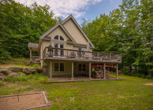 A two-story house with a balcony, surrounded by a wooded area.