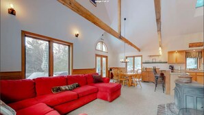 A spacious living room with a red sofa, wooden beams, large windows, a dining area, and a kitchen with wooden cabinets. - Walk to pond / playground in pet friendly chalet while enjoying mountain views (Madison)