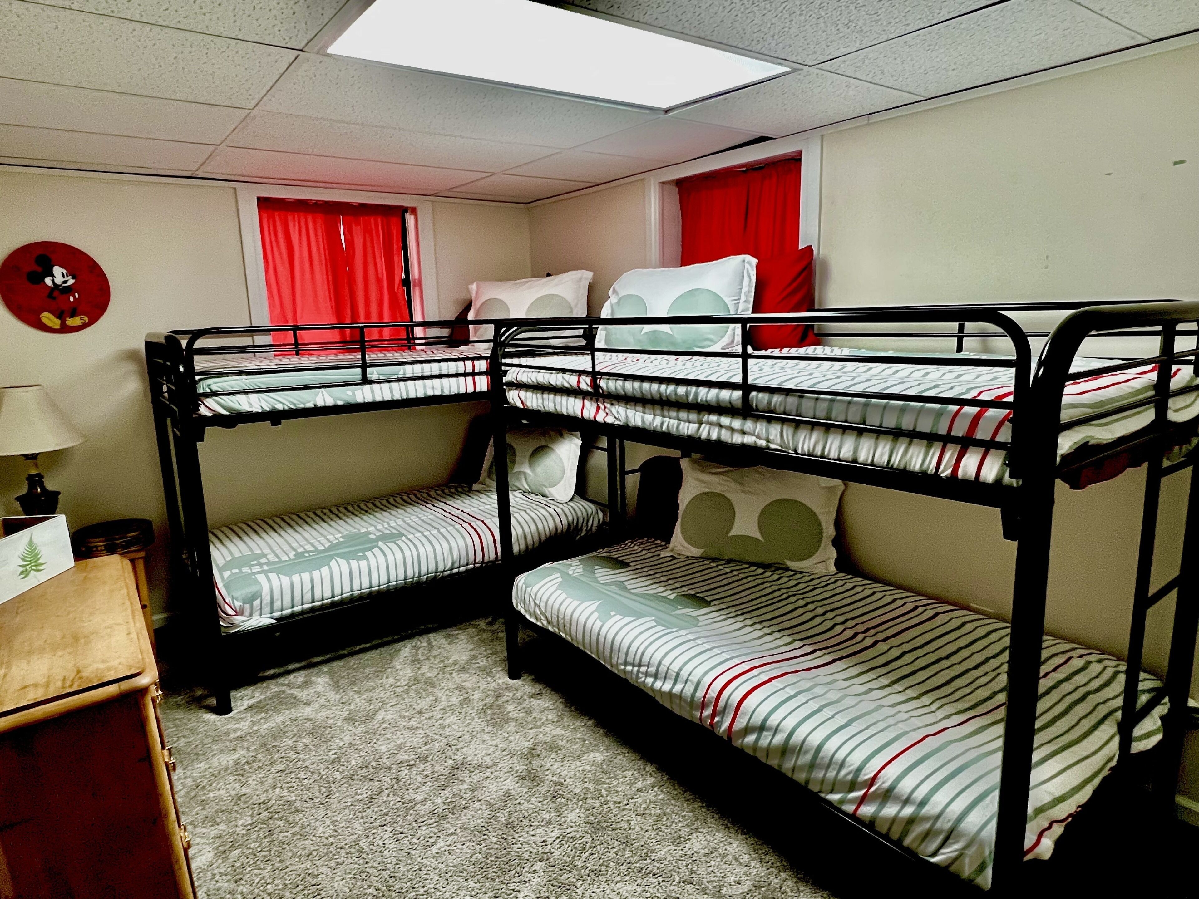 A bunk bed room with a red curtain, a lamp, and a Mickey Mouse wall decoration.