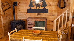 A wooden cabin interior with a dining table, chairs, a fireplace, and a staircase. - Rustic, small and primitive cabin - Riverview Cabin, LLC (Muscoda)