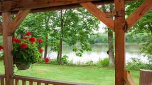 A wooden deck with a hanging flower pot and a view of a lake surrounded by trees. - Rustic, small and primitive cabin - Riverview Cabin, LLC (Muscoda)