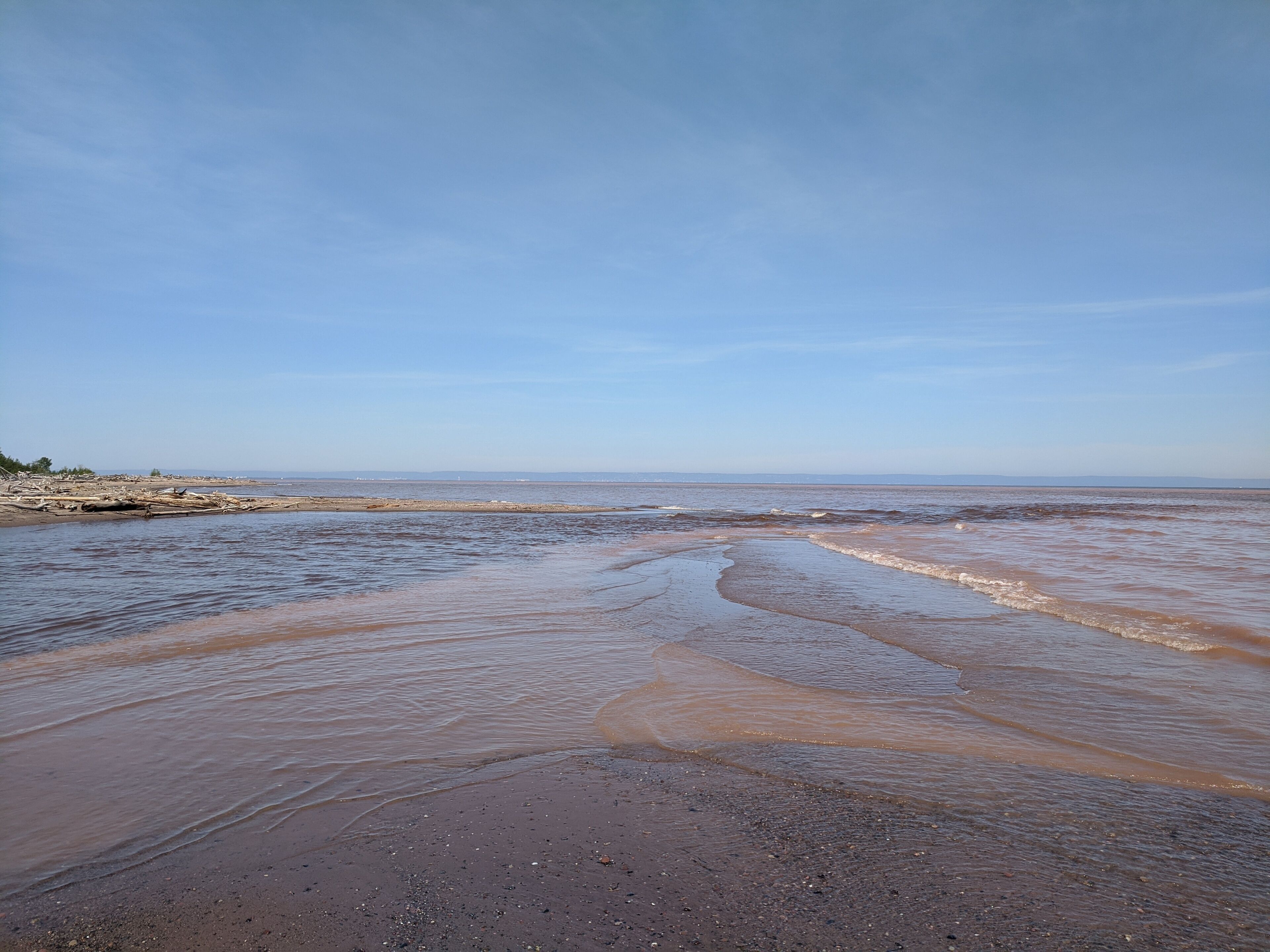 A beach with wet sand and gentle waves, a clear sky, and a distant shoreline.