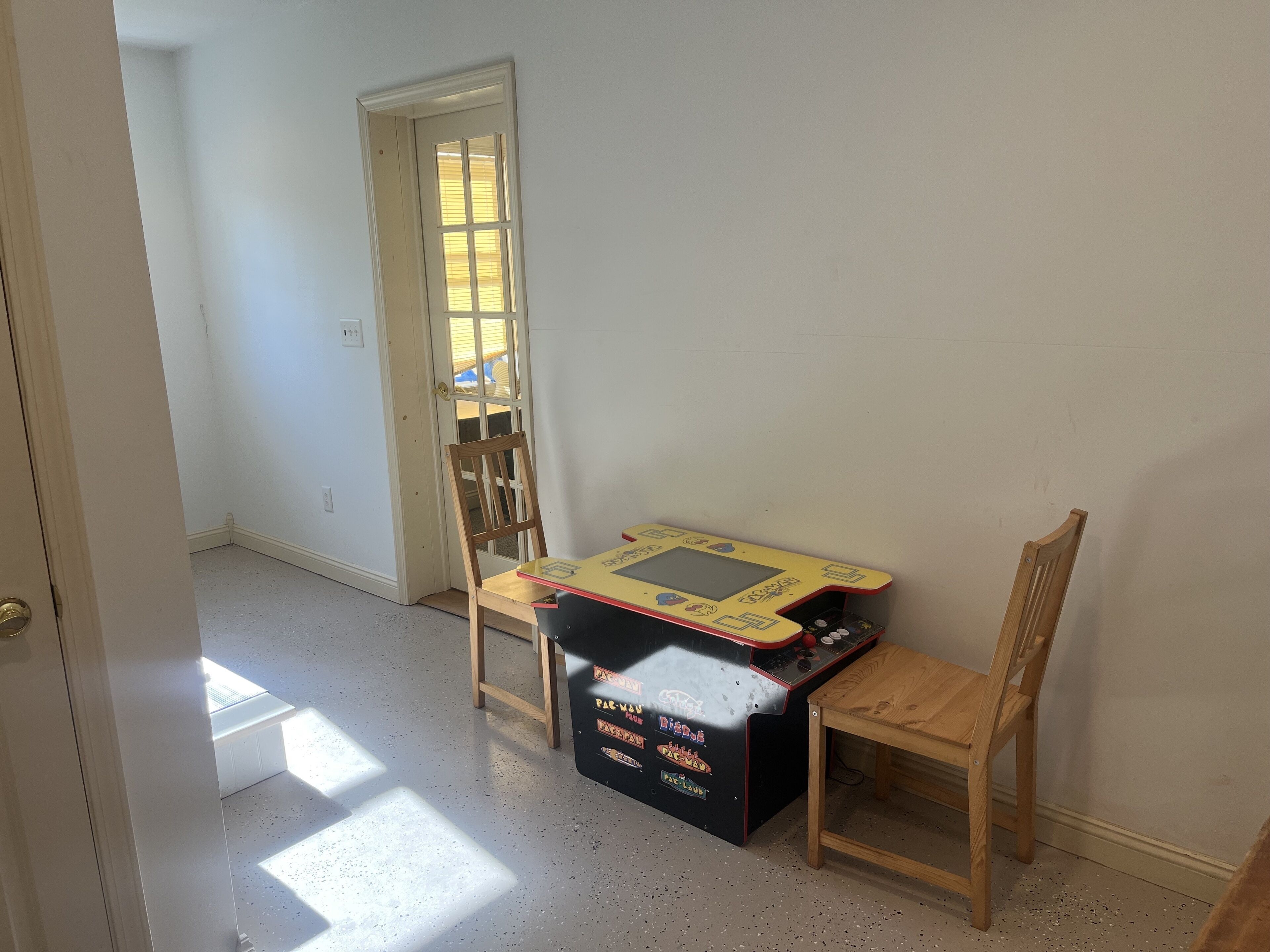 Una habitación con una mesa de madera, una silla y una máquina arcade de Pac-Man.
