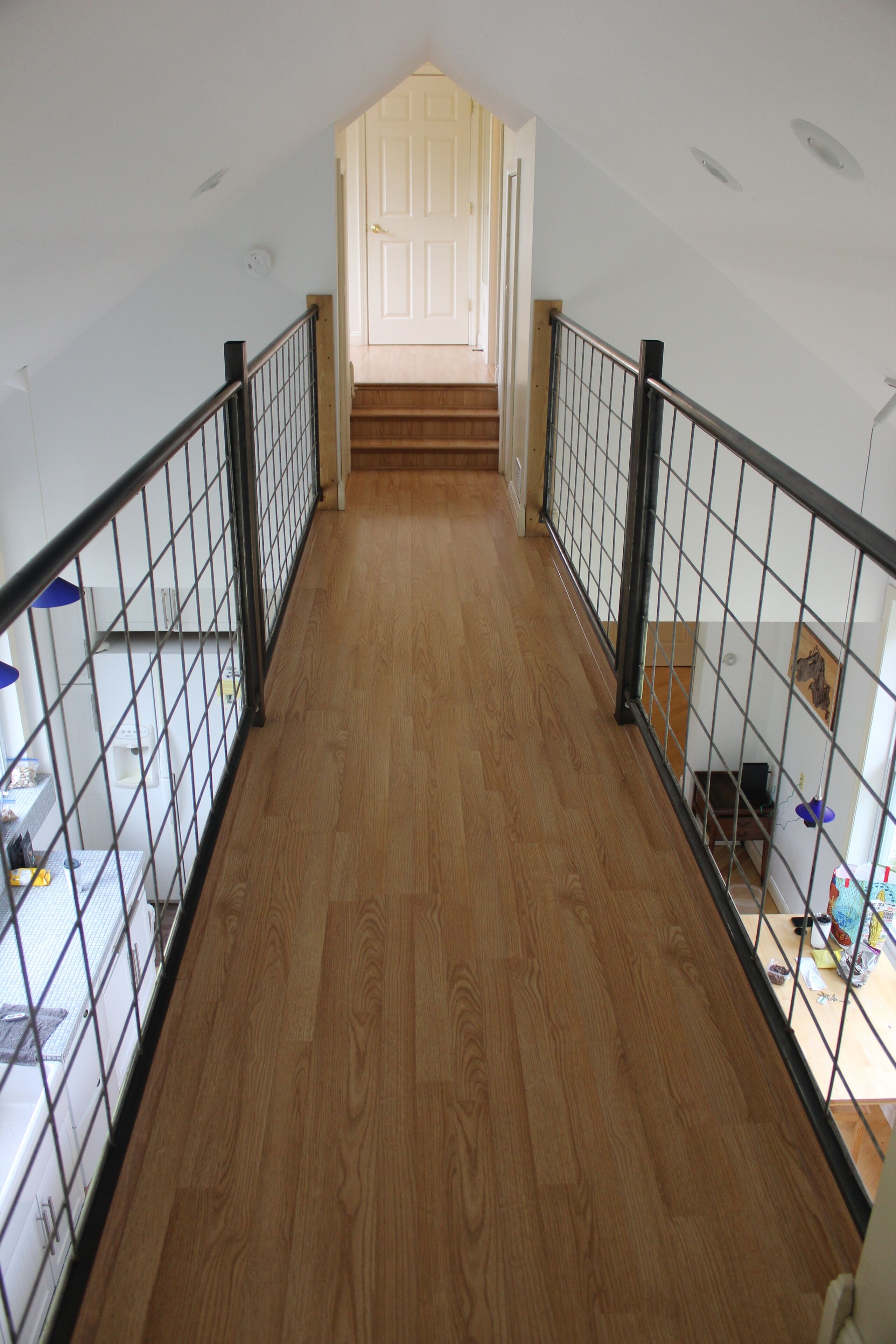 A wooden-floored corridor with a metal railing, leading to a door at the end.