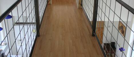 A wooden-floored corridor with a metal railing, leading to a door at the end.